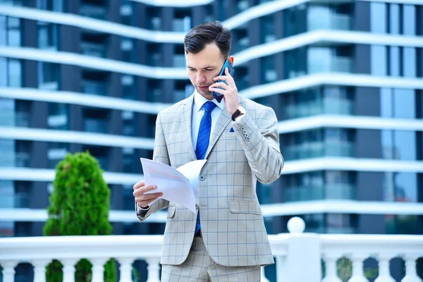 Akıllı telefondan konuşan ve iş raporlarını elinde tutan genç bir iş adamı. İş ve yatırım kavramı.