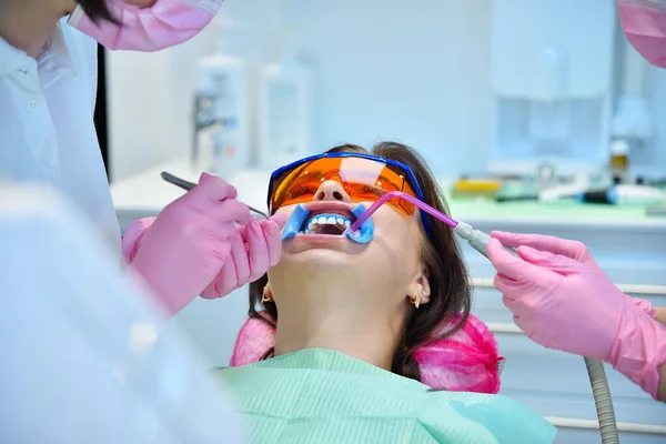 Dentist with assistant prepares woman patient for teeth whitening procedure in dental office. Dental and teeth whitening concept.