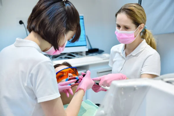 Woman patient with protective glasses and retractor for teeth whitening procedure in clinic. Bleaching of teeth at dentist clinic. Dental and teeth whitening concept.