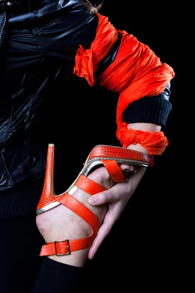 Mano de mujer, envuelta en una bufanda naranja, sosteniendo una pierna en un zapato naranja — Foto de Stock