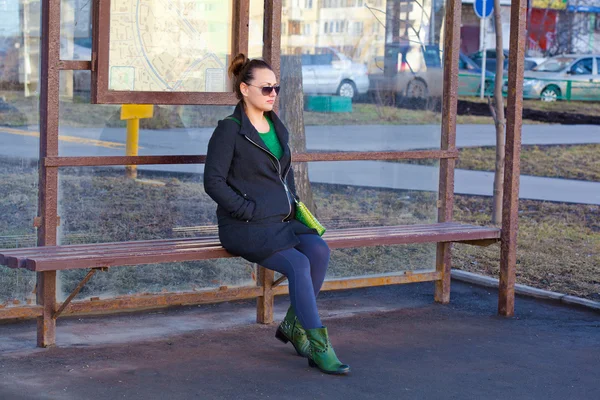 Chica sentada en un banco esperando transporte en la parada de autobús —  Fotos de Stock