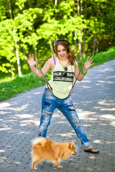 Chica divertida en camiseta y jeans escuchando música con auriculares al aire libre con su perro —  Fotos de Stock