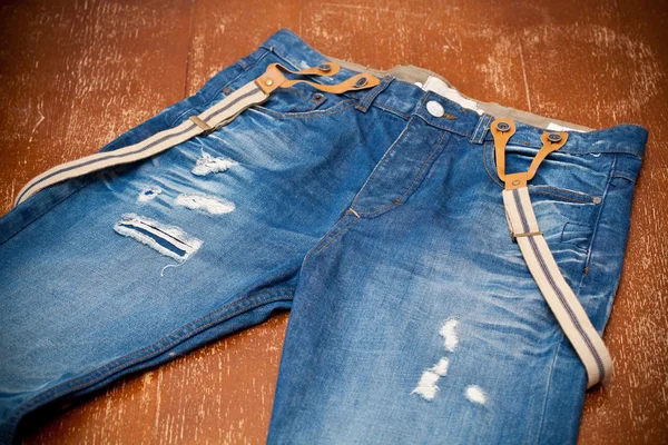 Worn blue jeans with holes and suspenders — Stock Photo, Image