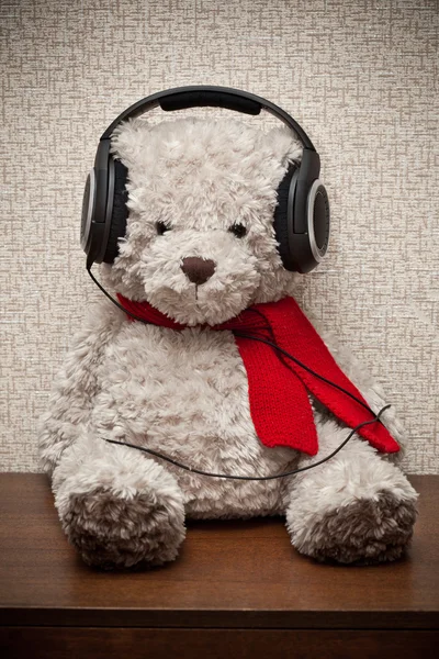 Teddy bear with a red scarf listening to music on headphones — Stock Photo, Image