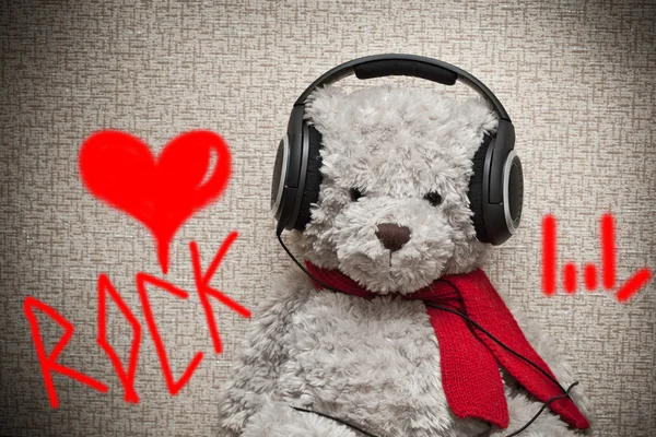 Toy teddy bear with a red scarf listening to music on headphones. Fan of Rock music — Stock Photo, Image