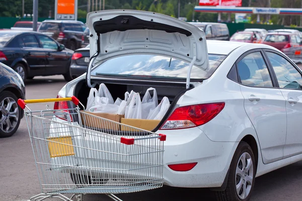 Les sacs à provisions sont dans le coffre de la voiture et le chariot d'épicerie Images De Stock Libres De Droits