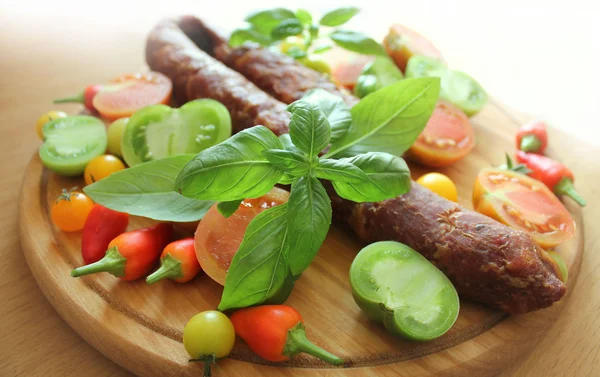 Sausage,peppers, basil and tomato on a wooden cutting board — Stock Photo, Image