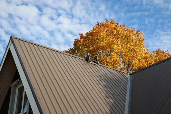 Maison de toit en métal brun sous l'arbre autmn contre le ciel bleu — Photo