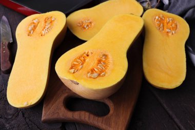 Tahta kesme tahtasının üzerinde yarım tereyağlı kabak. Arka planda bıçak ve mutfak havlusu.