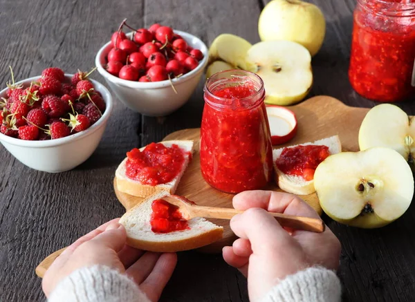 Glazen pot met verschillende soorten bessen en fruit op houten tafel. Appel, frambozen, meidoornjam — Stockfoto