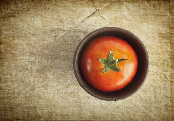 Röd söt tomat i en lera kopp över gamla papper bakgrund — Stockfoto