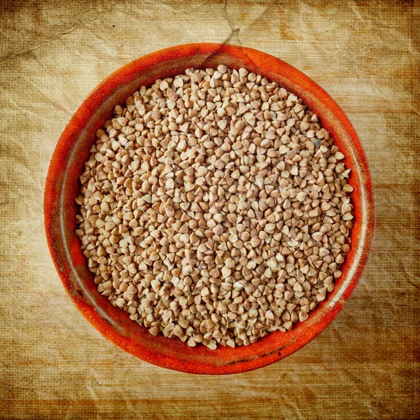 Buckwheat in a ceramic bowl over old paper background — Stock Photo, Image