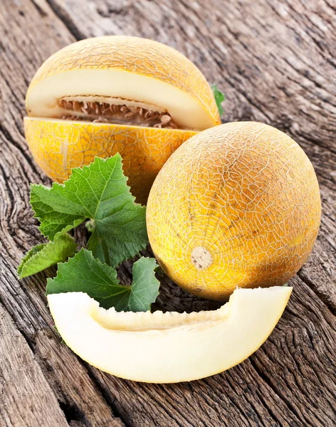 Melon avec tranches et feuilles sur une vieille table en bois . — Photo