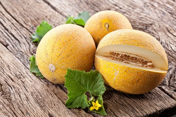 Melón con rodajas y hojas sobre una vieja mesa de madera . —  Fotos de Stock