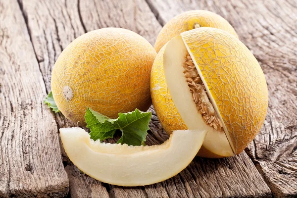 Melón con rodajas y hojas sobre una vieja mesa de madera . —  Fotos de Stock