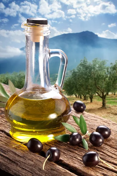 Zwarte olijven met fles van olie op een houten tafel. — Stockfoto