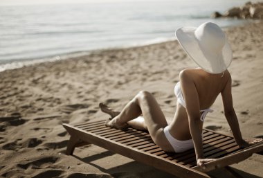 genç kadın şezlong üzerinde oturan sunbathes.