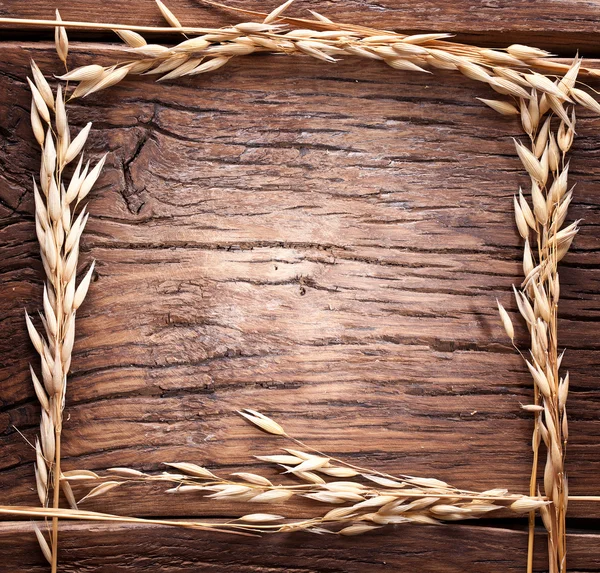 Ears of wheat made as frame on old wooden table. — Stock Photo, Image