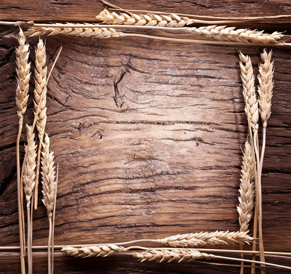 Ears of wheat made as frame on old wooden table. — Stock Photo, Image