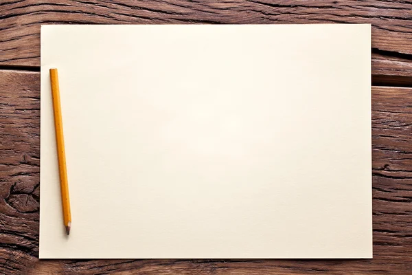 Hoja blanca de papel y lápiz sobre una vieja mesa de madera . —  Fotos de Stock