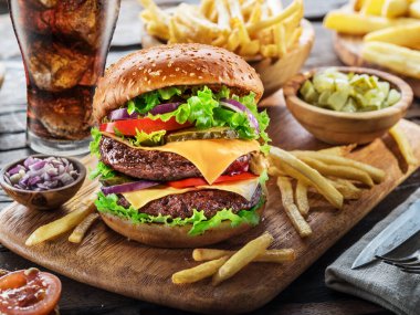 Tahta zemin üzerinde kola ve patates kızartması olan nefis bir çizburger. Fast food konsepti.