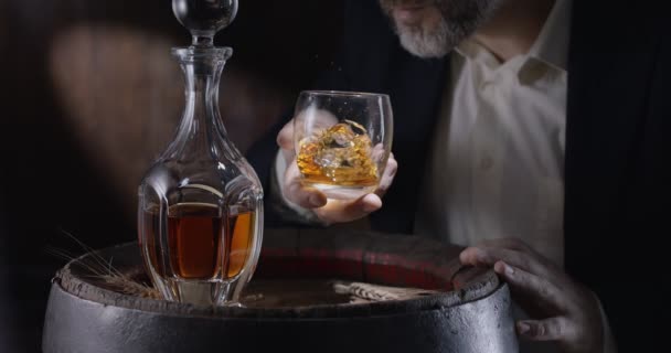 スーツを着た男と髭 ソムリエ ヴィンテージのウイスキー樽から氷の上にウイスキーのグラスを取り ガラスを振るとウイスキーの香りが広がります スローモーション4K 150 Fps Blackmagic Ursa Pro — ストック動画