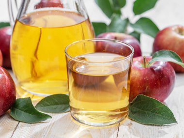 Bir bardak meyve suyu, bir sürahi taze elma suyu ve ahşap masada organik elmalar..