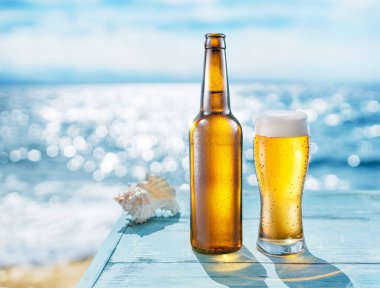 Bira şişesi ve bira bardağının ahşap masanın üzerinde buğulanmış hali. Arka planda bulanık bir deniz var. Yaz titreşimleri.