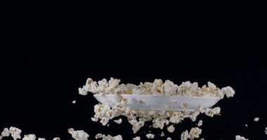 Patlamış mısır, beyaz bir plakayla birlikte siyah bir zemine doğru yavaşça uçar.. 