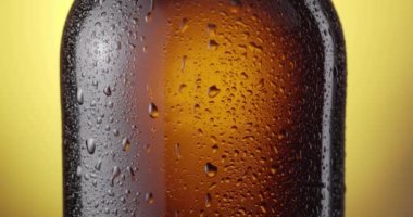 Kamera, ortasından kahverengi, sisli bira şişesinin boynuna kadar sarı arka planda hareket ediyor. Bir damla buğulanma aşağı akar..