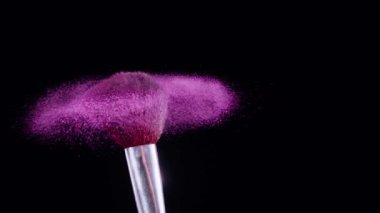 Makyaj fırçası titrer ve ince pembe toz parçacıkları oluşturur. Siyah arka plan, yavaş çekim, 300 fps.