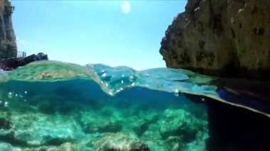 Hava ve su sınırında ağır çekim yarı su altı videosu. Karadağ 'da Adriyatik Denizi üzerindeki güzel kayalık plaj.