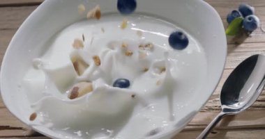 Taze yaban mersinli tahıl gevreği kahvaltısı (granola) sabah ışığında yavaşça yoğurdun içine düşer. 300fps