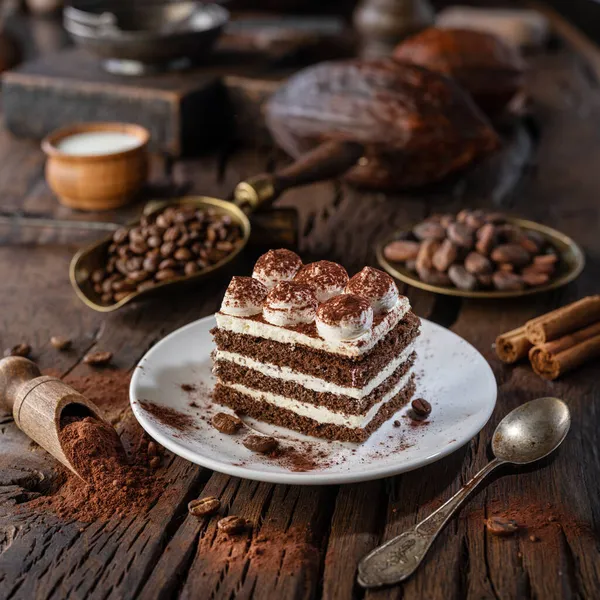 木製のテーブルの上にティラミスクリームとココアパウダーとチョコレートケーキのスライス — ストック写真