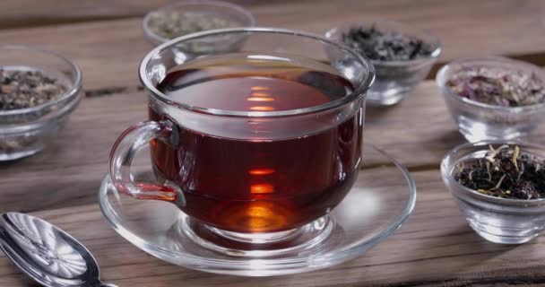 慢慢地掉进一杯茶里 周围有小碗 里面有不同类型的叶茶 老式木桌 — 图库视频影像