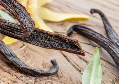 Kurutulmuş vanilya meyveleri ve tahta masada vanilya orkidesi. Yakın plan..