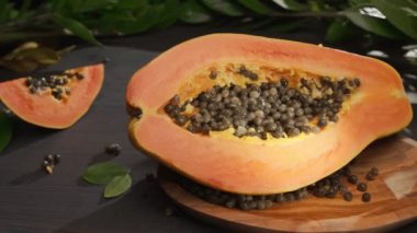 Yarım papaya meyvesi ve tropikal bitki yapraklarıyla birlikte antika bir masa üzerinde tohum. Bir el, bir kase meyvenin üzerine bir parça papaya koyar. Kameranın soldan sağa yatay yavaş hareketi. 