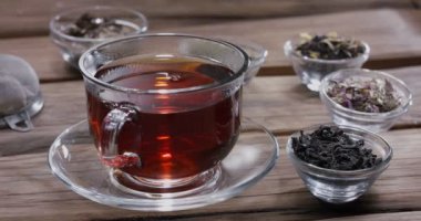 Damla yavaşça bir bardak çaya düşer. Etrafta farklı yaprak çayları olan küçük kaseler var. Klasik ahşap masa.. 