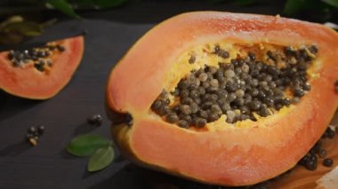 Yarım papaya meyvesi ve tropikal bitki yapraklarıyla birlikte antika bir masa üzerinde tohum. Bir el, bir kase meyvenin üzerine bir parça papaya koyar. Kameranın soldan sağa yatay yavaş hareketi. 