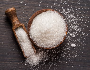 Tahta kasede beyaz rafine şeker ve koyu ahşap masada kaşık. 