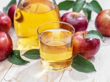 Bir bardak meyve suyu, bir sürahi taze elma suyu ve ahşap masada organik elmalar..