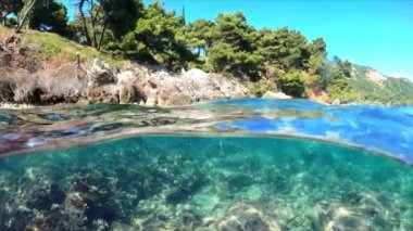 Hava ve su sınırında ağır çekim yarı su altı videosu. Karadağ 'da Adriyatik Denizi üzerindeki güzel kayalık plaj.