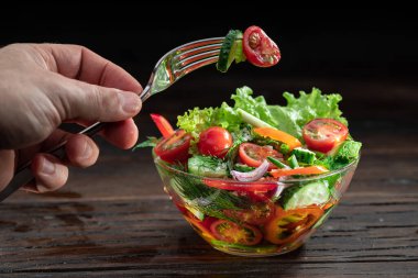 Vegetable salad with leafy greens in the glass oil is on the wooden table. clipart