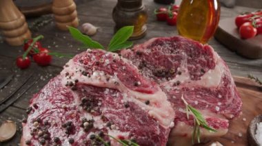 Ahşap mutfak masasında baharatlı ve otlu iki çiğ kaburga bifteği. Kamera mutfak masasının etrafında yavaşça hareket ediyor.. 