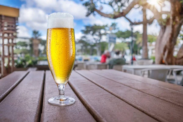 木製のテーブルの上にビールの冷たいガラス 背景には外に広がる夏のストリートカフェ — ストック写真