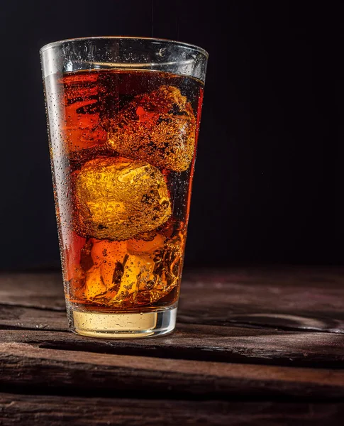 Chilled glass of cola drink with ice cubes isolated on dark background.