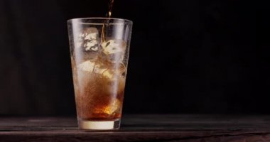 Kola buzlu bir bardak kolaya dökülür. Cam, siyah arka planı olan ahşap bir masanın üzerinde duruyor. Gaz kabarcıkları bardakta aktif olarak yükselir. 