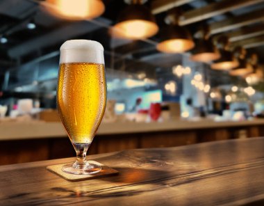 Cooled glass of beer with condensate on the wooden table. Blurred bar at the background. clipart