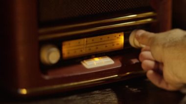 Klasik ahşap retro radyo alıcısı, radyo dalgalarının elle ayarlandığı makro çekim, akort düğmesini döndüren el. Soldan sağa yavaş kamera hareketi.