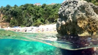 Hava ve su sınırında ağır çekim yarı su altı videosu. Karadağ 'da Adriyatik Denizi üzerindeki güzel kayalık plaj.
